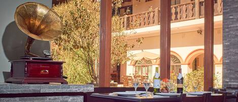 An outdoor dining area with a table set for two, a gramophone, and wine bottles.