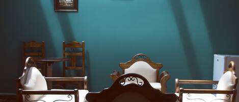 A room with teal walls, two wooden chairs with white cushions, and a wooden table.