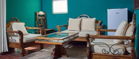 A room with teal walls, wooden furniture, a glass-top coffee table, and a white refrigerator.