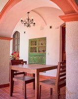 Un comedor con una mesa y sillas de madera, un armario verde con botellas y una araña.