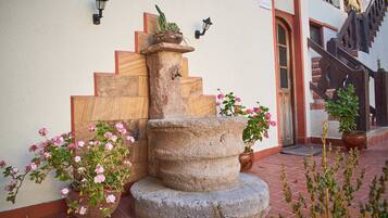 A stone fountain with a wooden staircase leading up to a door, surrounded by potted plants and flowers.