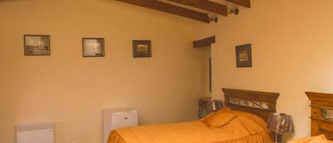 A bedroom with a bed, a nightstand, a lamp, and a small table. There are three framed pictures on the wall.