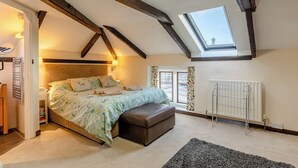 A bedroom with a sloped ceiling, a skylight, a bed with floral bedding, a radiator, and a window with curtains. - Orchard Cottage - UK30437 (Langport, near Somerton)