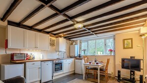 A compact kitchen with white cabinets, a built-in oven, a toaster, and a sink. There is a dining table with chairs, a leather sofa, and a television. - Orchard Cottage - UK30437 (Langport, near Somerton)