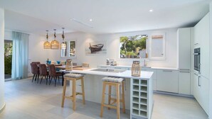 Een moderne keuken met een centraal eiland, barkrukken, hanglampen en een eethoek met stoelen en een tafel.