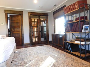 A room with a bed, a patterned rug, a bookshelf with books, and a door leading to another room.
