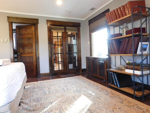 A room with a bed, a patterned rug, a bookshelf with books, and a door leading to another room.