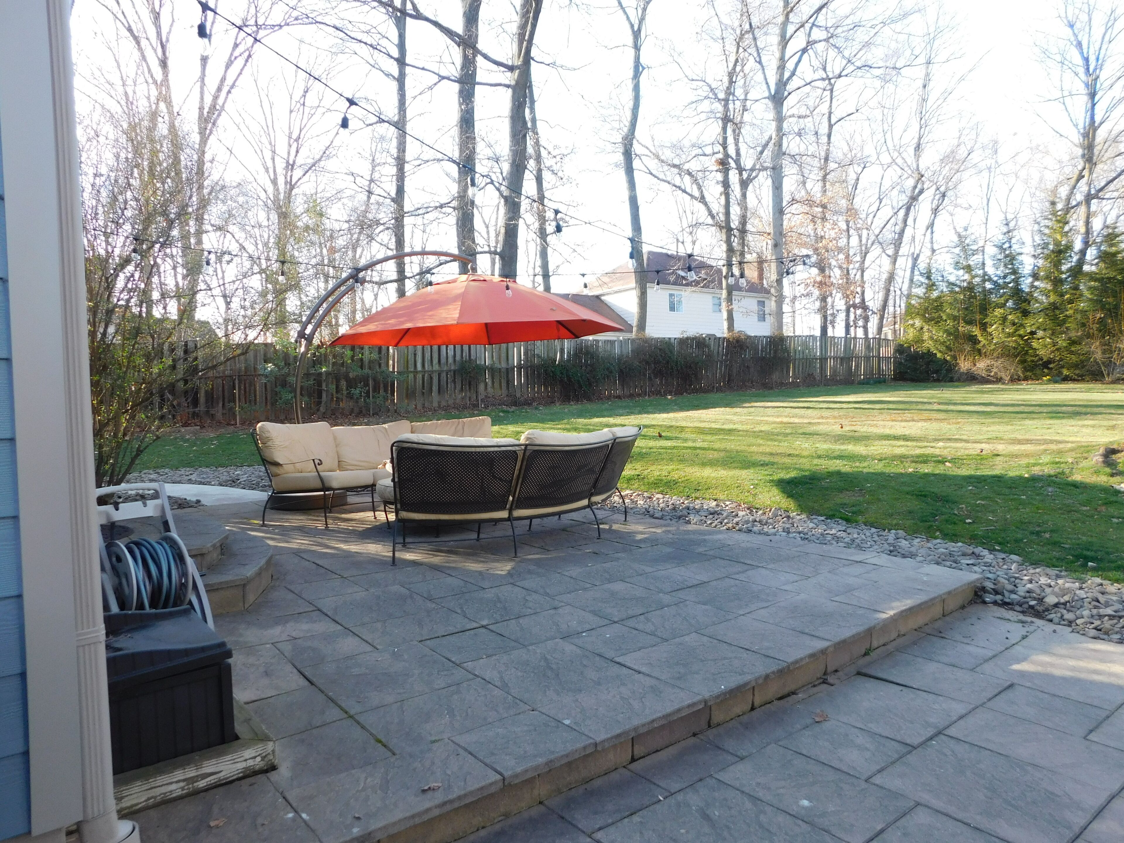A patio with a table and chairs, an umbrella, and a view of the backyard.