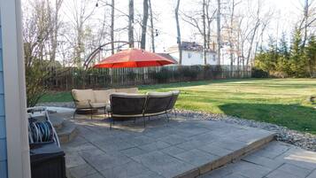 A patio with a table and chairs, an umbrella, and a view of the backyard.