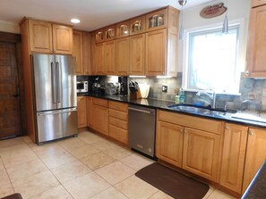 A kitchen with wooden cabinets, stainless steel appliances, a black countertop, and a window with a view.