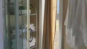 A bathroom with a glass shower enclosure, a towel rack with white towels, and a window with curtains.
