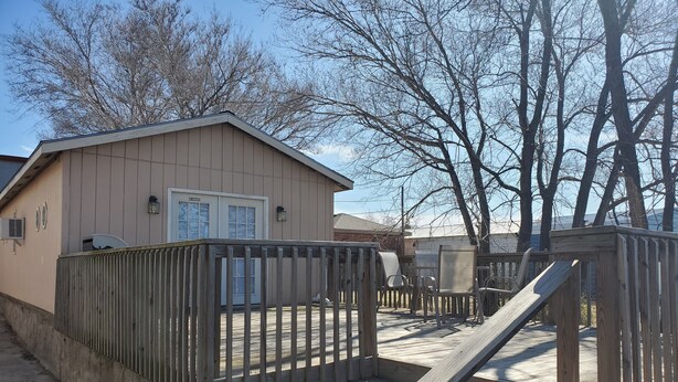 A wooden deck with a staircase leading to a building with a beige exterior and a white door.