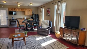 A living room with a fireplace, a television, a dining area with chairs, and a kitchen with wooden cabinets and appliances.