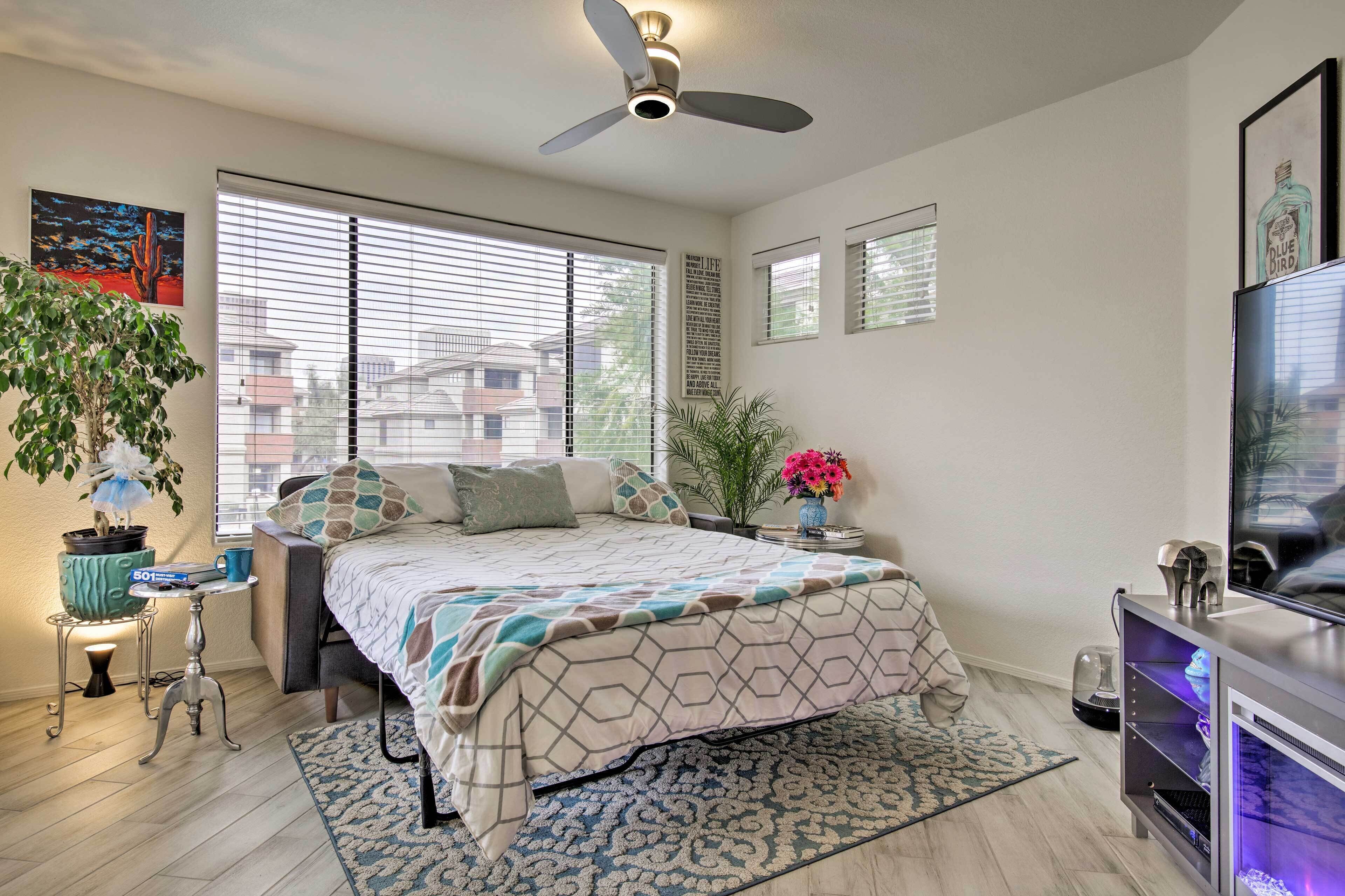 A bedroom with a bed, a ceiling fan, a TV, and a window with blinds.