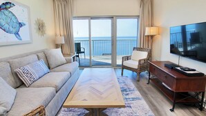 Une chambre d’hôtel avec un canapé, une table à manger, une télévision et un balcon donnant sur la mer.