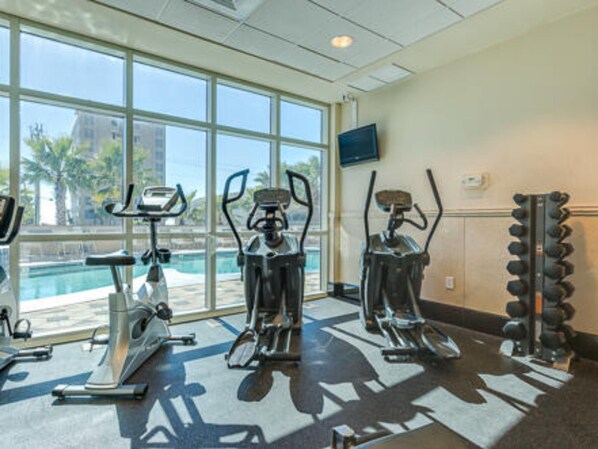 A gym with exercise equipment and a large window overlooking a pool.