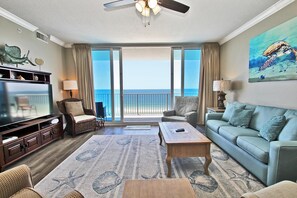 A spacious living room with a large flat-screen TV, comfortable seating, a wooden coffee table, and a view of the ocean through large sliding doors. - San Carlos 609 (Gulf Shores)