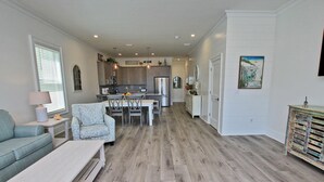 A spacious living area with a dining table, a sofa, and a coffee table. A kitchen with modern appliances is visible in the background.
