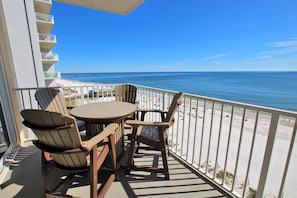 A balcony with a table and chairs overlooking a beach.