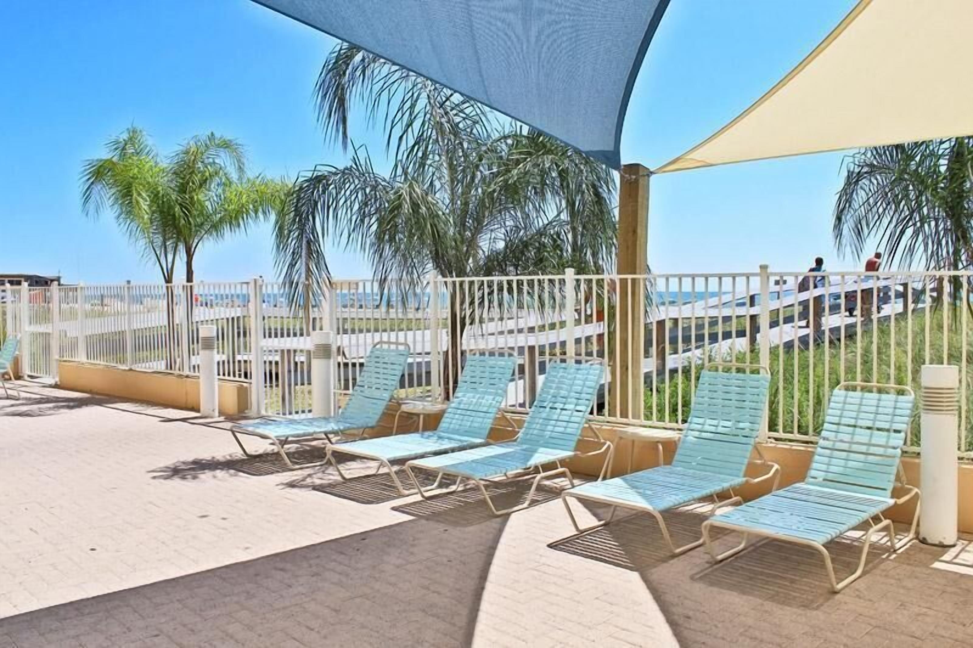 A covered outdoor seating area with lounge chairs and a view of the beach.