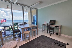 A balcony with a view of the ocean, a dining table with chairs, a desk with a computer, and a rug on the floor. - San Carlos 701 (Gulf Shores)