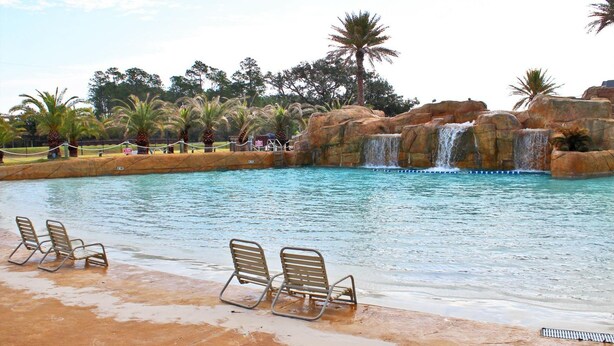 A pool with a waterfall, lounge chairs, and palm trees.