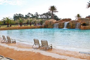 A pool with a waterfall, lounge chairs, and palm trees. - The Wharf 902 by Youngs Suncoast (Orange Beach)