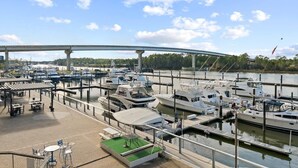 A marina with multiple boats docked, a covered seating area, and a bridge in the background.
