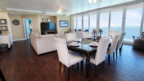 A dining area with a view of the ocean, a living room with a TV, and a kitchen with a clock. - San Carlos Penthouse 5 (Gulf Shores)