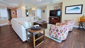 A living room with a sofa, a coffee table, a TV, and a patterned armchair. - San Carlos Penthouse 5 (Gulf Shores)