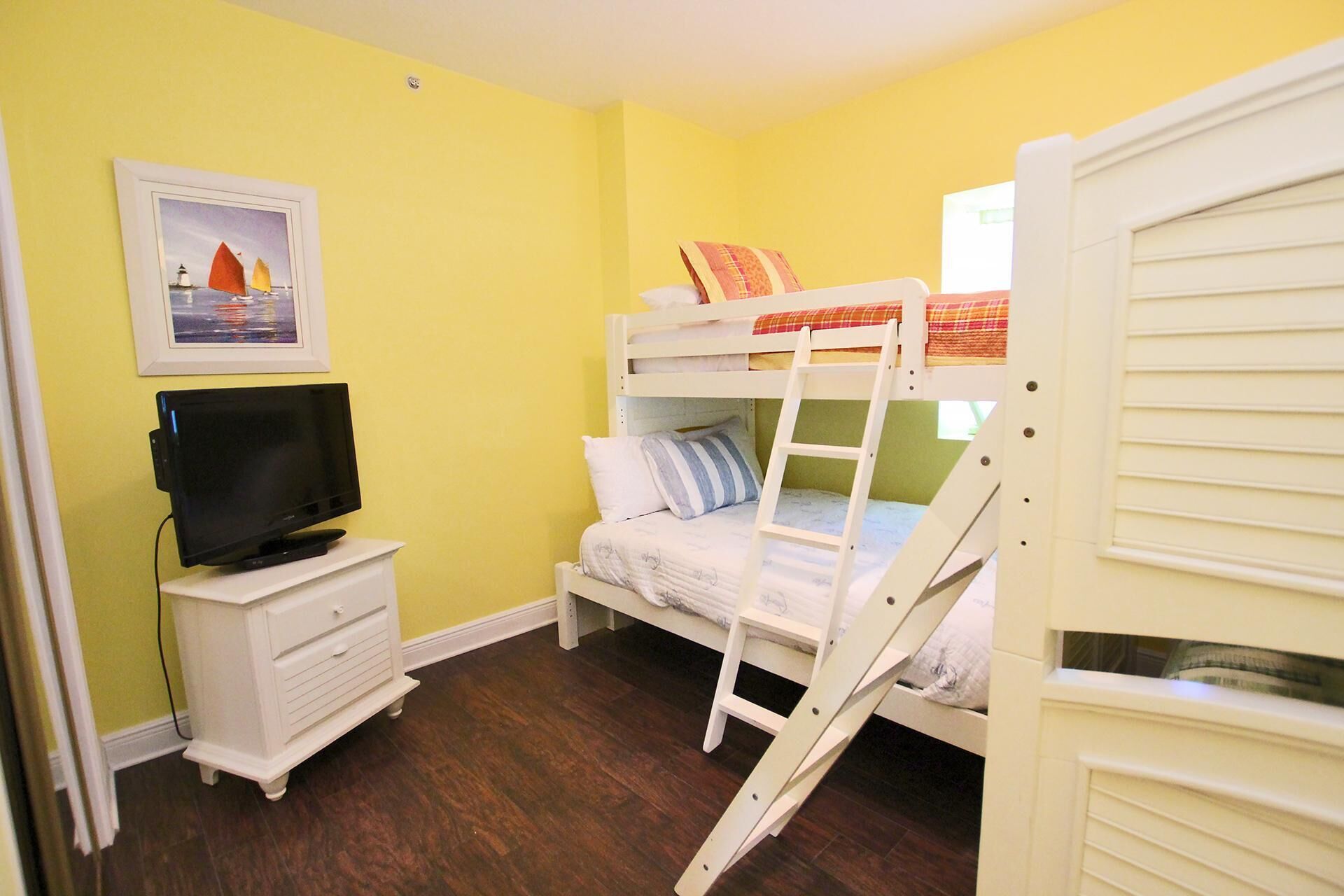 A room with a bunk bed, a TV on a white cabinet, and a painting on the wall.