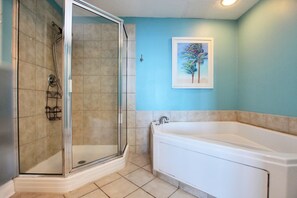 A bathroom with a glass shower enclosure, a bathtub, and a wall-mounted painting of a tree.