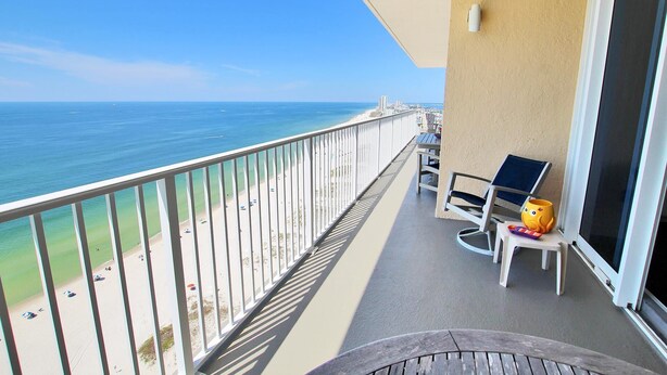 A balcony with a view of the beach and ocean. There are two chairs and a small table with a cup and a toy on it. - San Carlos Penthouse 5 (Gulf Shores)