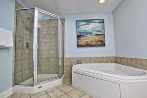 A bathroom with a glass-enclosed shower, a bathtub, and a painting on the wall.