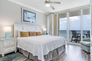 A bedroom with a large bed, a ceiling fan, a nightstand with a lamp, and a view of the ocean through a sliding glass door. - San Carlos 808 (Gulf Shores)