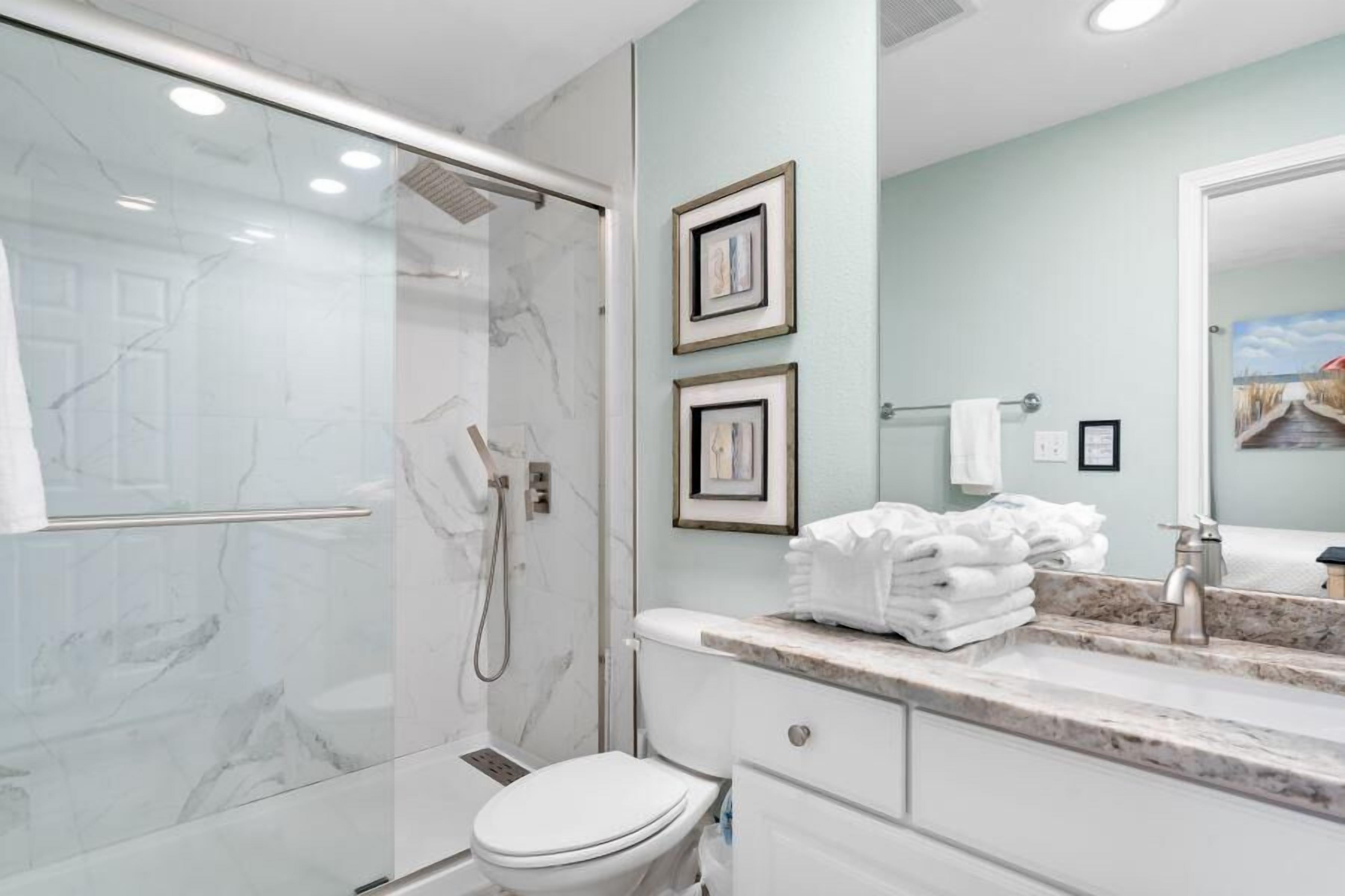 Une salle de bain moderne avec une douche à parois de verre, des toilettes blanches et un plan de toilette en marbre avec un lavabo et un miroir.