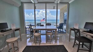 A room with a large table and chairs, a computer desk, and a view of the ocean through large windows. - San Carlos 401 (Gulf Shores)