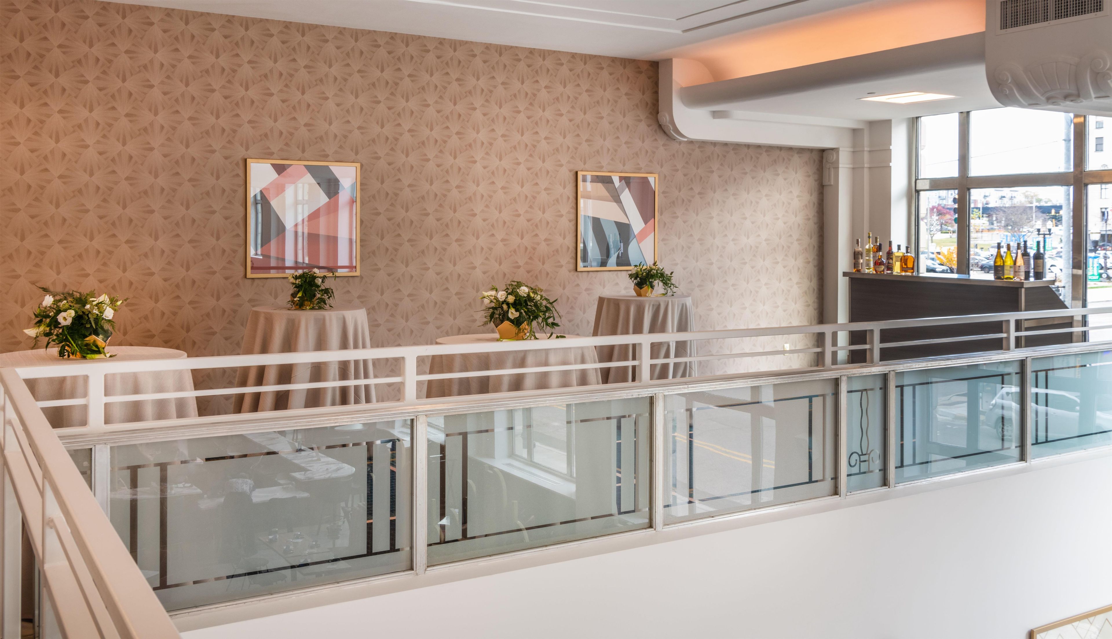 Un hall d’hôtel doté d’une rambarde en verre, de deux tables ornées de compositions florales et d’œuvres d’art accrochées aux murs.