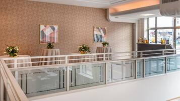 Un hall d’hôtel doté d’une rambarde en verre, de deux tables ornées de compositions florales et d’œuvres d’art accrochées aux murs.
