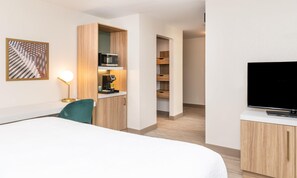 A hotel room with a bed, a desk with a coffee machine, a TV, and a painting on the wall. - Hilton Garden Inn Flint Downtown (Flint)