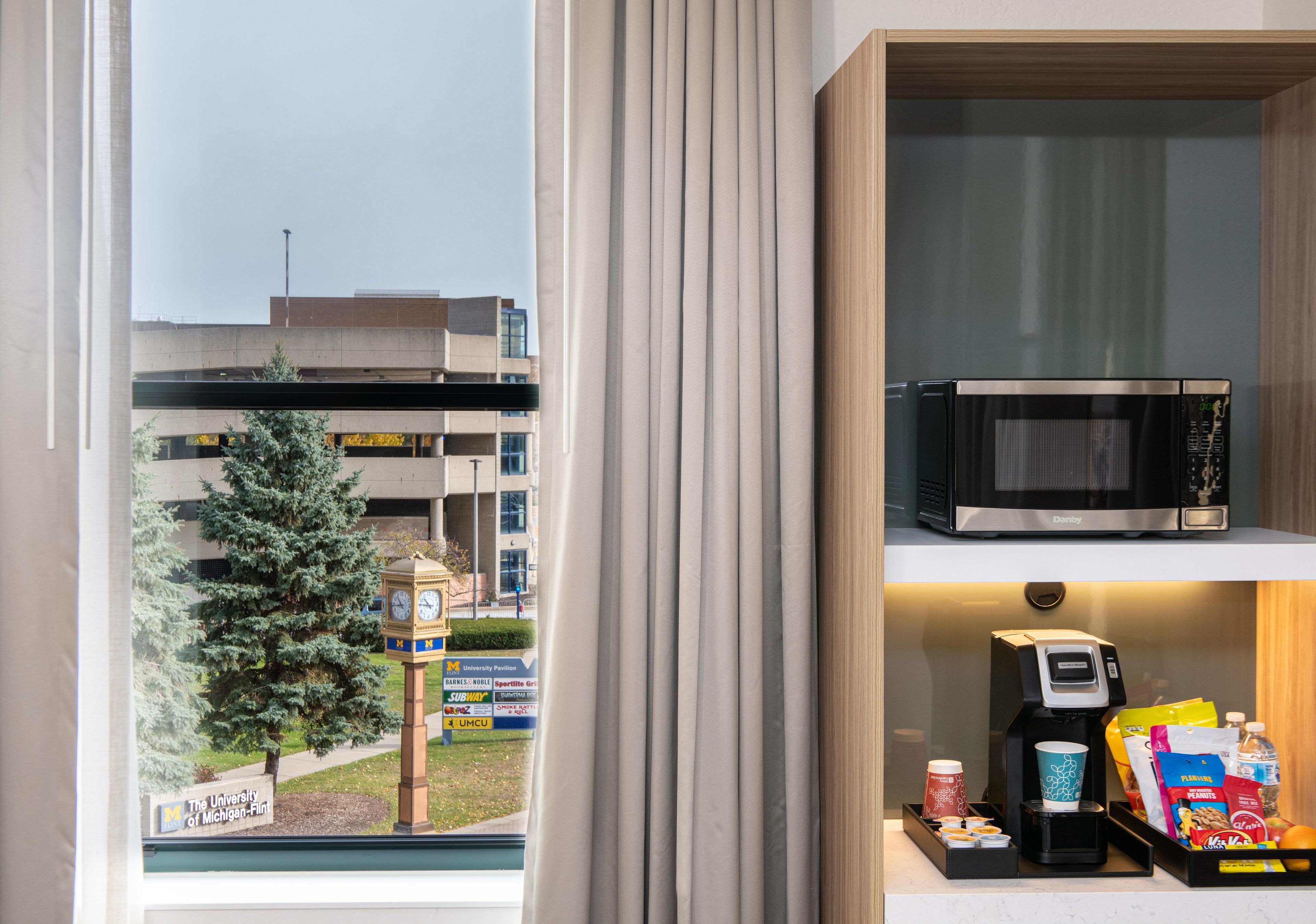 Habitación con vista al edificio de la universidad, un reloj, un microondas y una cafetera.