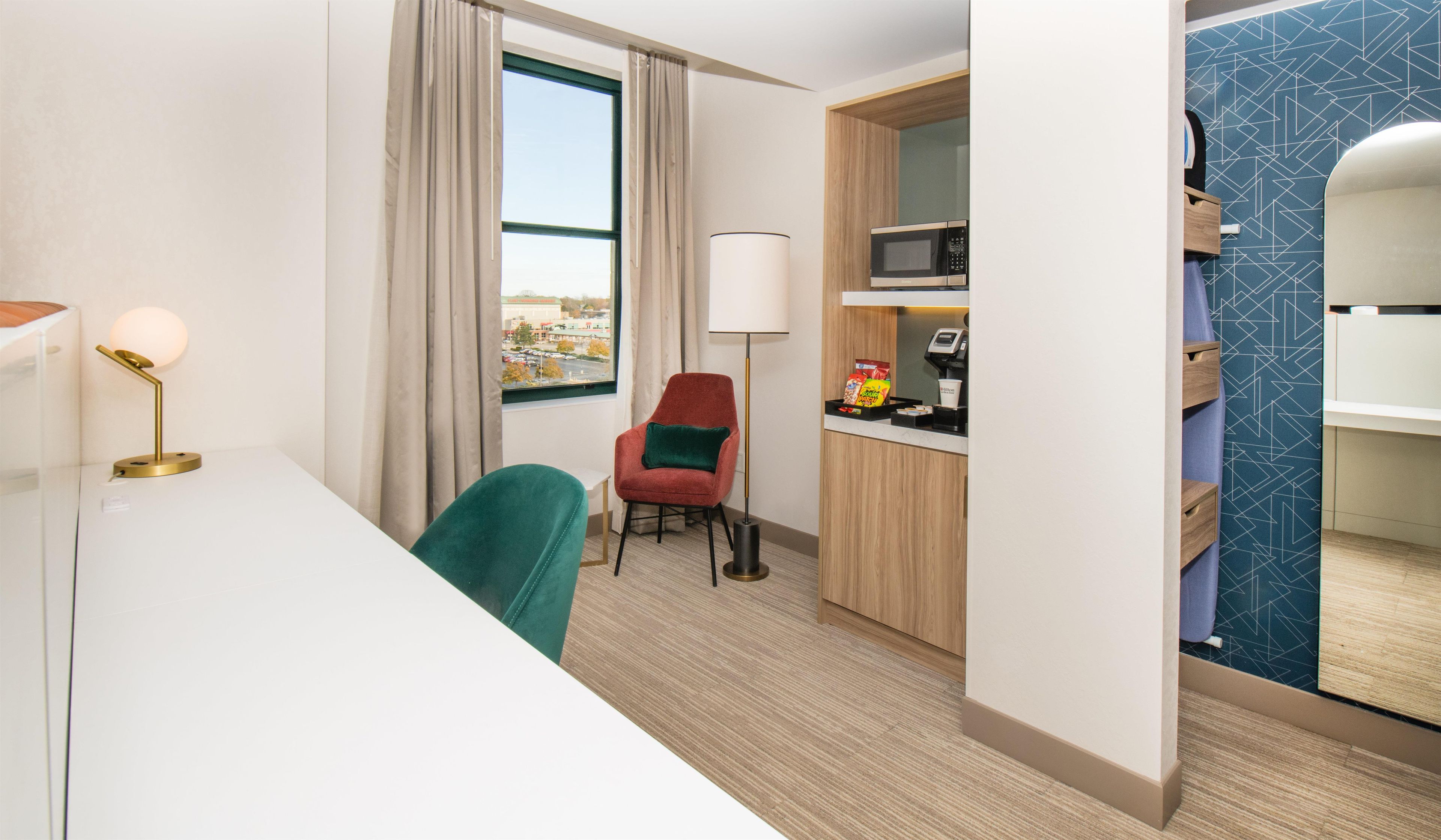 Hotellihuone, jossa on työpöytä, tuoli, lamppu, mikroaaltouuni ja näkymä kaupunkiin.