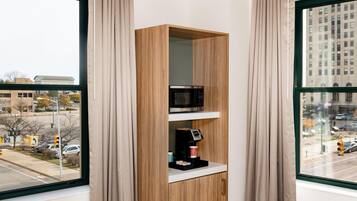Una habitación con una estantería de madera que contiene un microondas y una cafetera, una ventana con vistas a un paisaje urbano y una puerta con el cartel de estacionamiento 'P'.