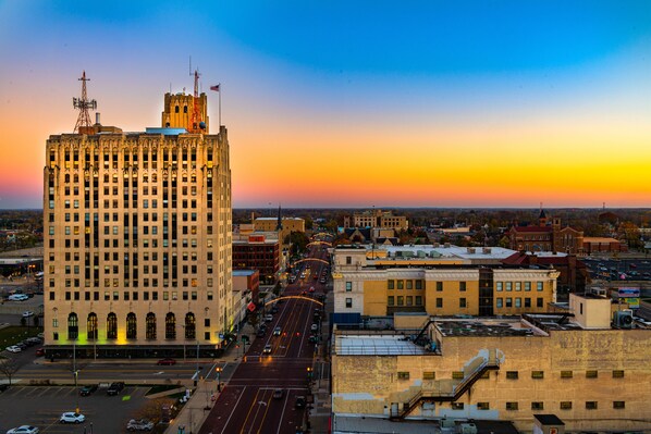 A cityscape with a prominent building featuring a large number of windows and a flag on top, surrounded by other buildings and a busy street. - Hilton Garden Inn Flint Downtown (Flint)