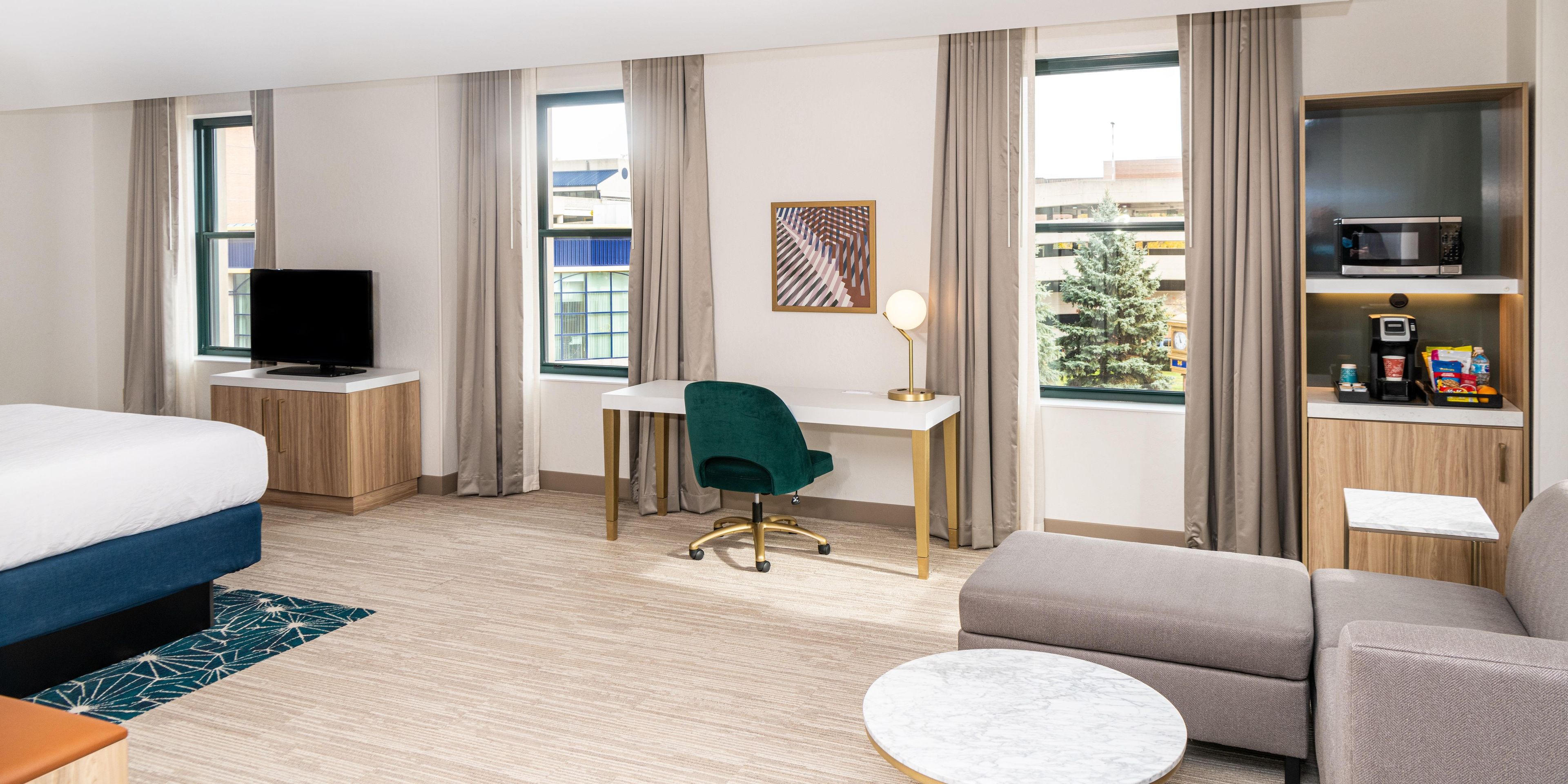 A hotel room with a bed, desk, chair, sofa, and a coffee machine.