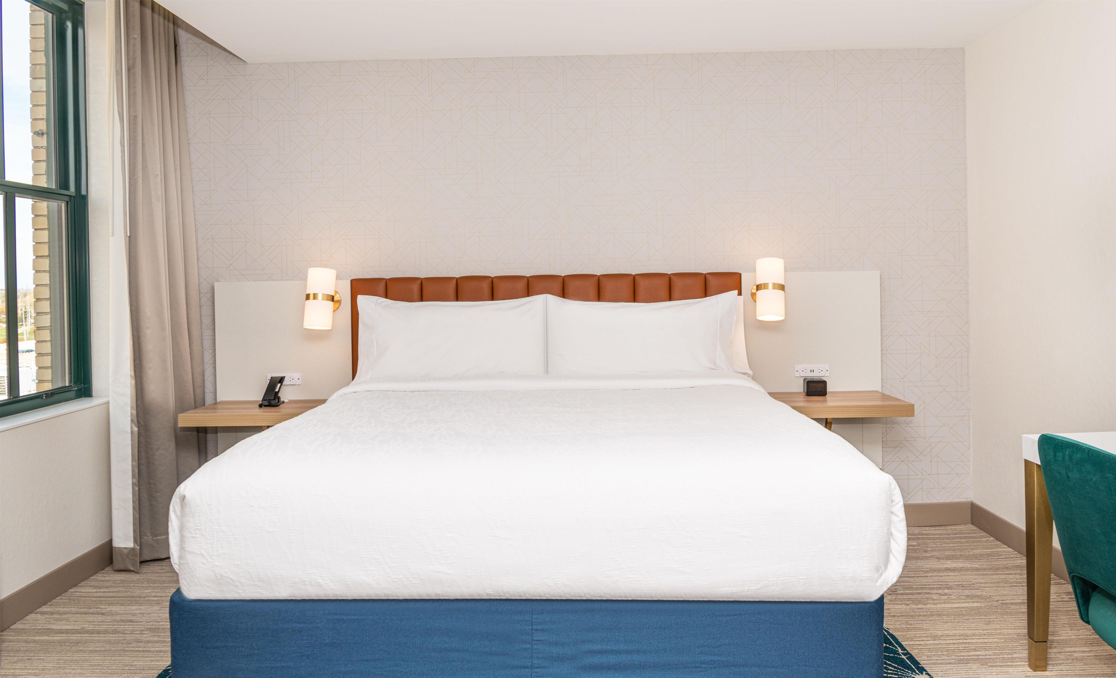 A hotel room with a large bed, two bedside tables, a nightstand, a desk, and a chair.