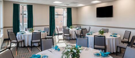 A conference room with round tables, chairs, and a flat-screen TV on the wall.