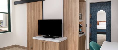 Una habitación moderna con una televisión sobre un mueble de madera, una mesa blanca y una silla color turquesa.