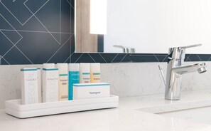 A bathroom vanity with a white soap dispenser holder containing various Neutrogena products. - Hilton Garden Inn Flint Downtown (Flint)