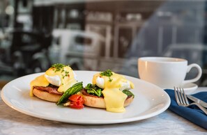 A breakfast plate with eggs benedict, greens, and a cup of coffee on a table with a blue napkin. - Hilton Garden Inn Flint Downtown (Flint)